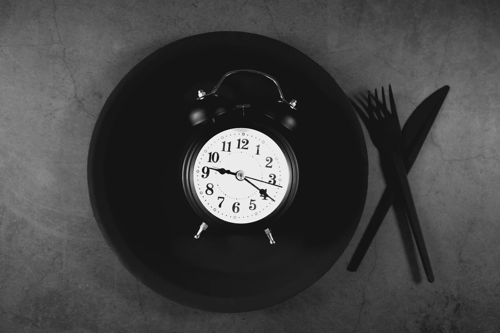 Alarm clock on an empty plate next to a knife and fork